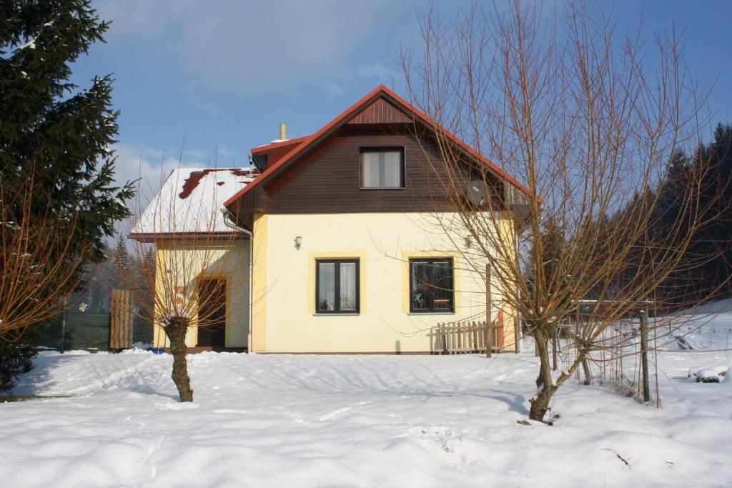 una casa amarilla con techo rojo en la nieve en Holiday House Arnultovice, en Rudník