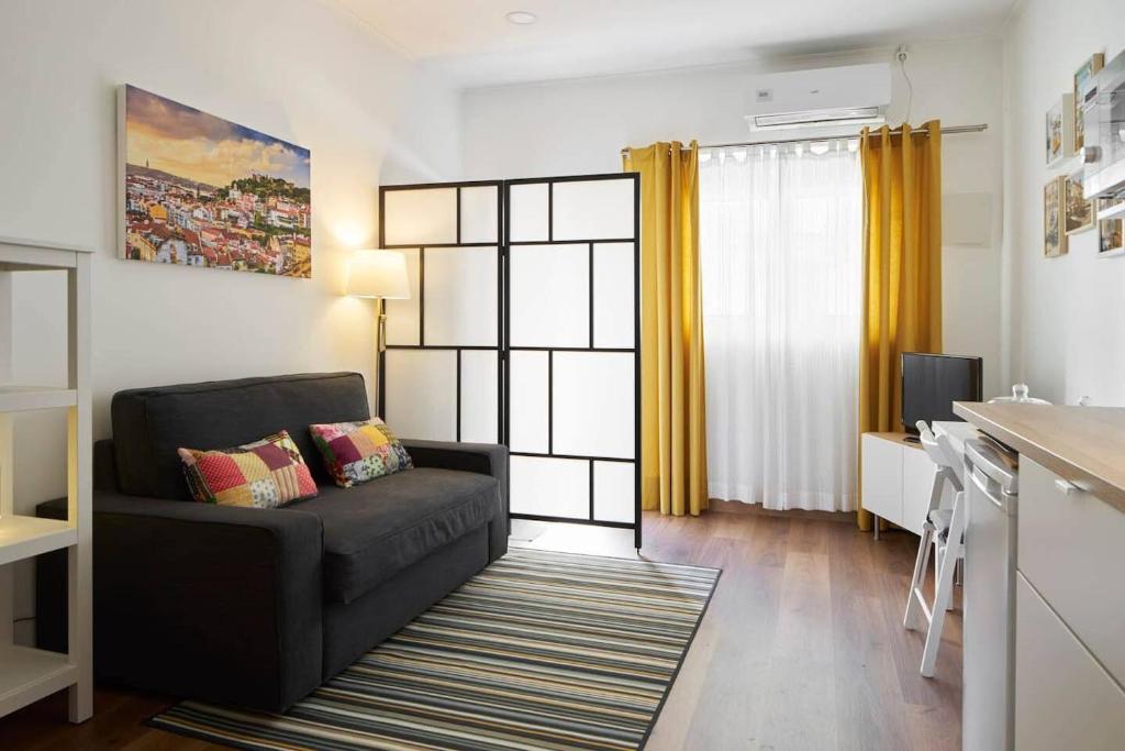 a living room with a black couch and a kitchen at Cozy Studio Alvalade in Lisbon