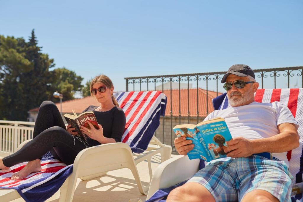 un hombre y una mujer sentados en sillas leyendo libros en Villa Kate Dadić, en Dubrovnik