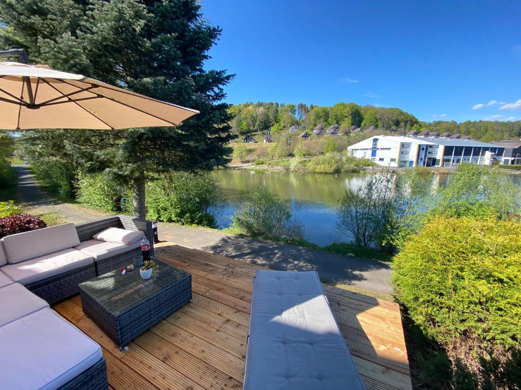 eine Holzterrasse mit einem Sofa und einem Sonnenschirm in der Unterkunft SEA Office - Modernes Ferienhaus mit tollem Seeblick in Kirchheim