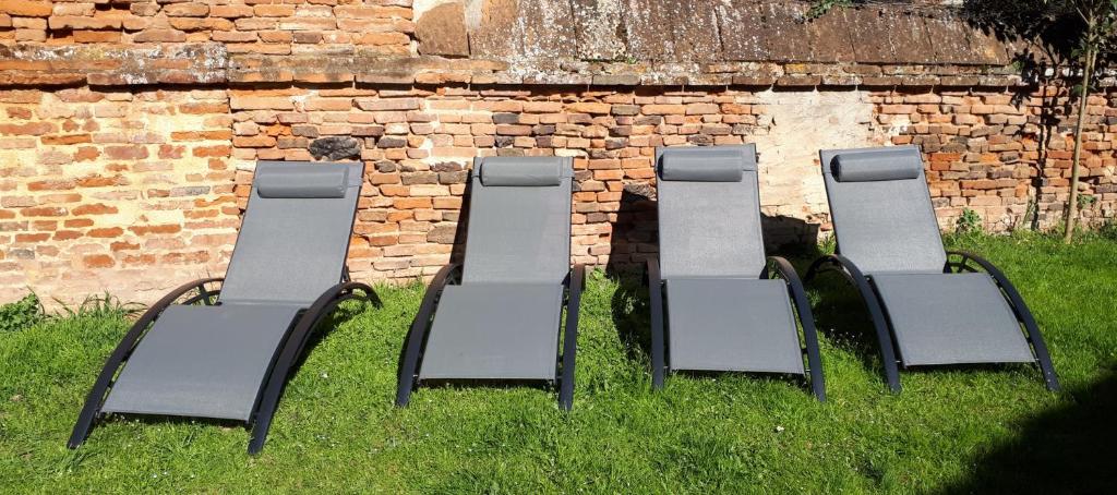 four chairs sitting in the grass next to a brick wall at Auberge des chemins in Moissac