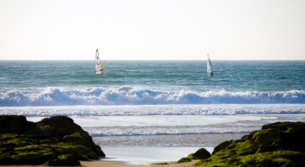 two sailboats in the ocean with a beach with waves at Hotel Fortaleza do Guincho Relais & Châteaux in Cascais