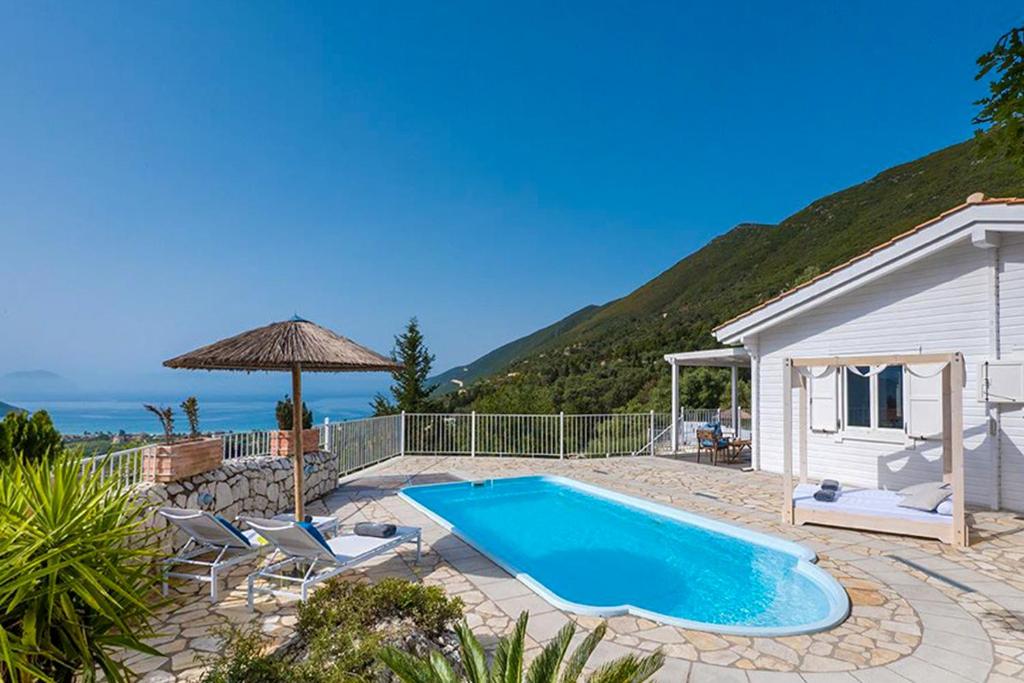 a swimming pool with chairs and an umbrella next to a house at Vasiliki Cottages in Vasiliki