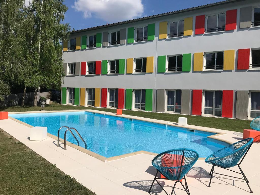 a swimming pool in front of a building at Hôtel Full Colors in Craponne