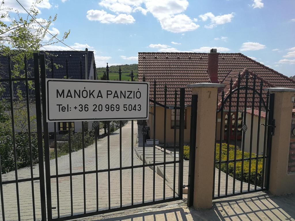 a gate with a sign in front of a building at Manoka Guest House in Mogyoród