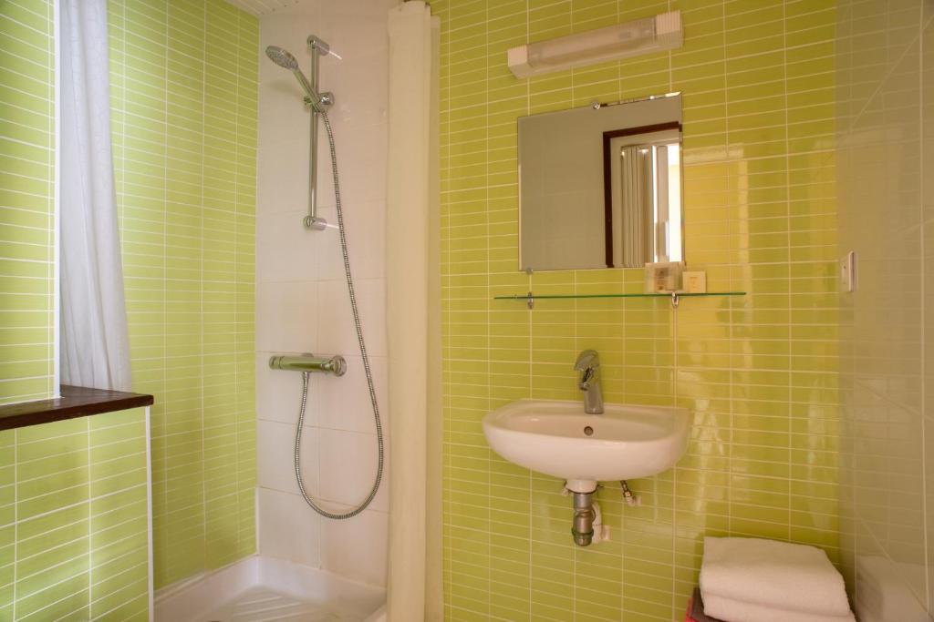 baño de azulejos verdes con lavabo y ducha en HotelLe MaraisCaillebotte, en Challans