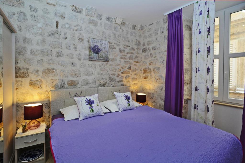a bedroom with a purple bed and a stone wall at L & L Old Town Apartments in Dubrovnik