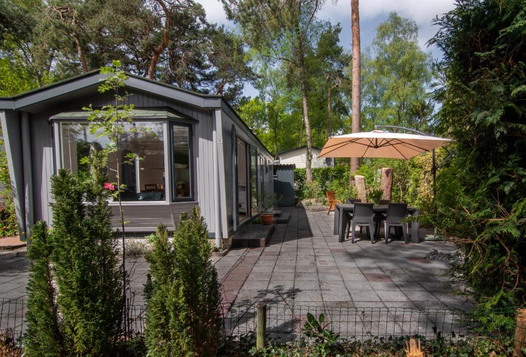 a tiny house with a patio and an umbrella at Luxe chalet op de Veluwe in Ermelo