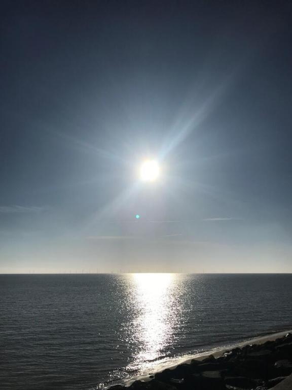 a sun is shining over the ocean with the water at Frinton Escapes in Frinton-on-Sea