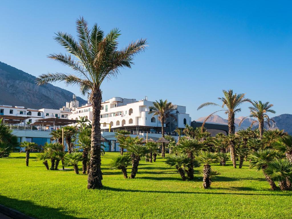 a group of palm trees in front of a building at Saracen Sands Hotel & Congress Centre - Palermo in Isola delle Femmine