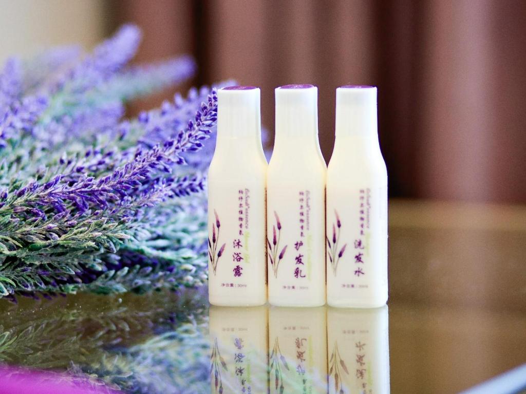 trois bouteilles blanches assises sur une table avec des fleurs violettes dans l'établissement Lavande Hotel Dongguan Humen Square, à Dongguan