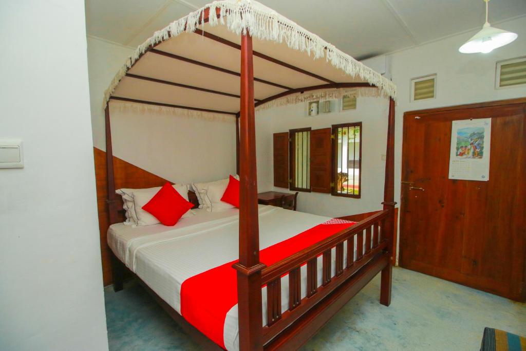 um quarto com uma cama de dossel em madeira com almofadas vermelhas em Hotel Nawathana em Matara
