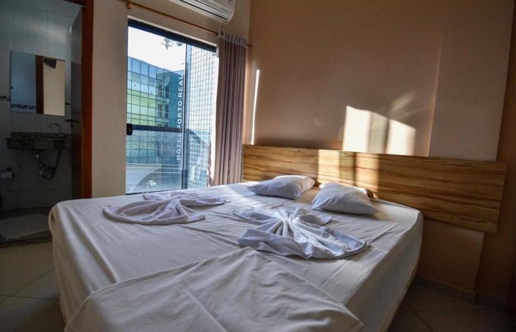 a bed with white sheets and pillows and a window at Hotel Mirante do Porto in Aparecida