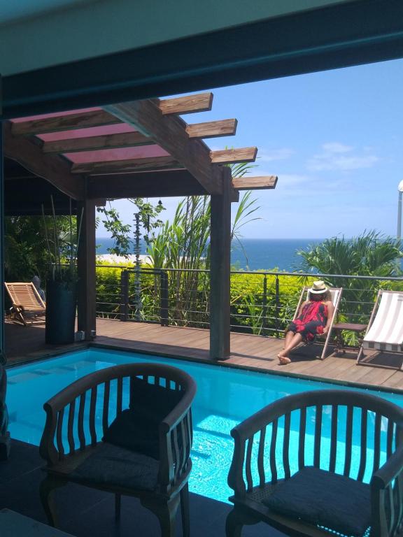 a woman sitting in a chair next to a swimming pool at Suite INDIGO JACUZZI PRIVE PISCINE VUE MER acces cuisine laverie in Saint-Pierre