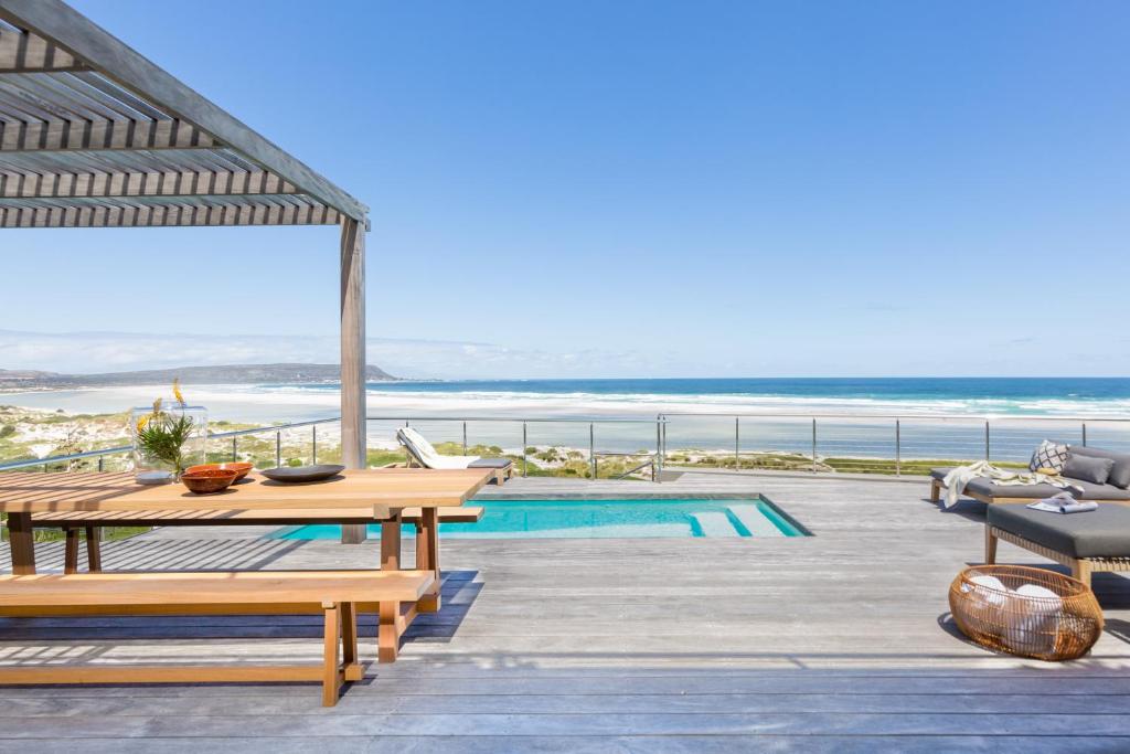 a patio with a table and benches and the ocean at Cape Beach Villa in Noordhoek