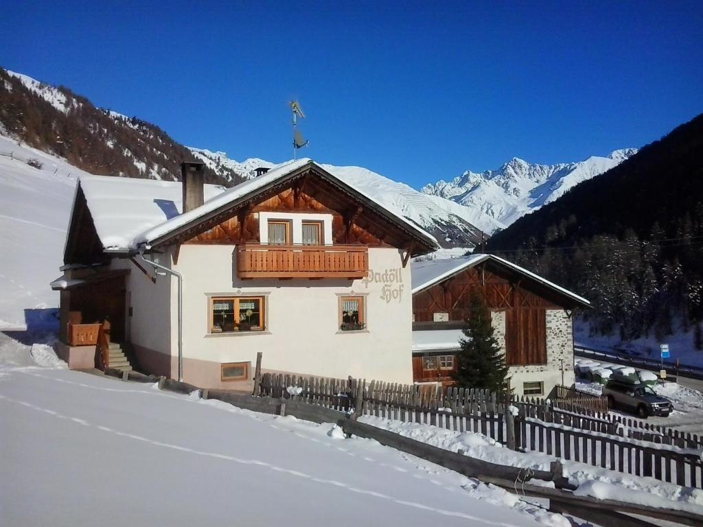 a house in the snow with a fence and mountains at Padoellhof in Curon Venosta