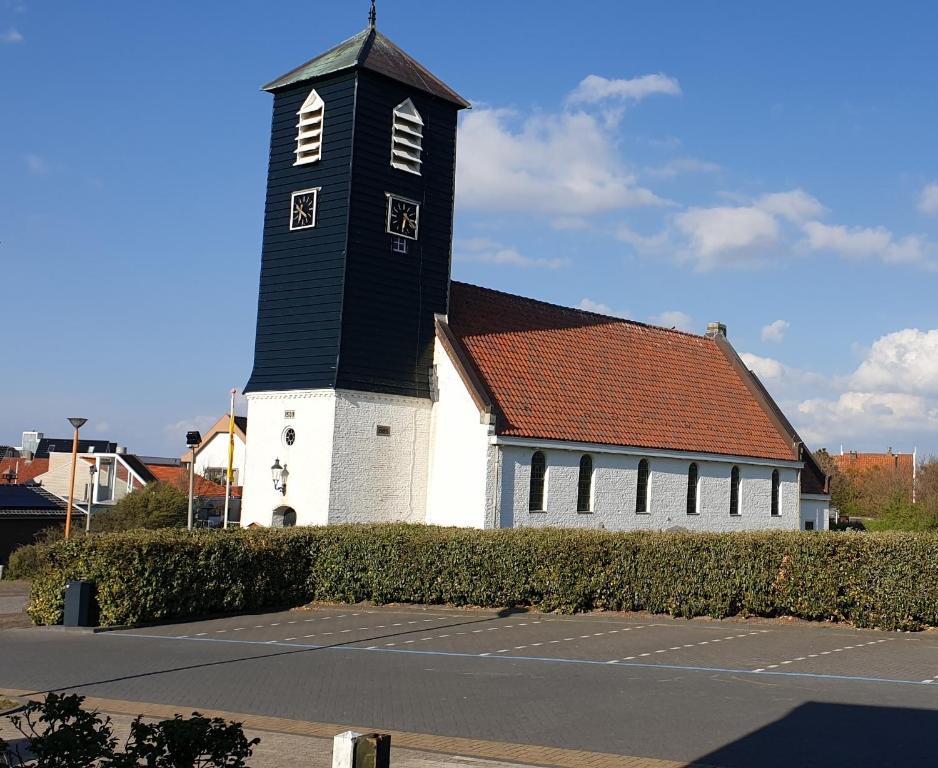 une église noire et blanche avec une grande tour dans l'établissement BzonderB Callantsoog, à Callantsoog