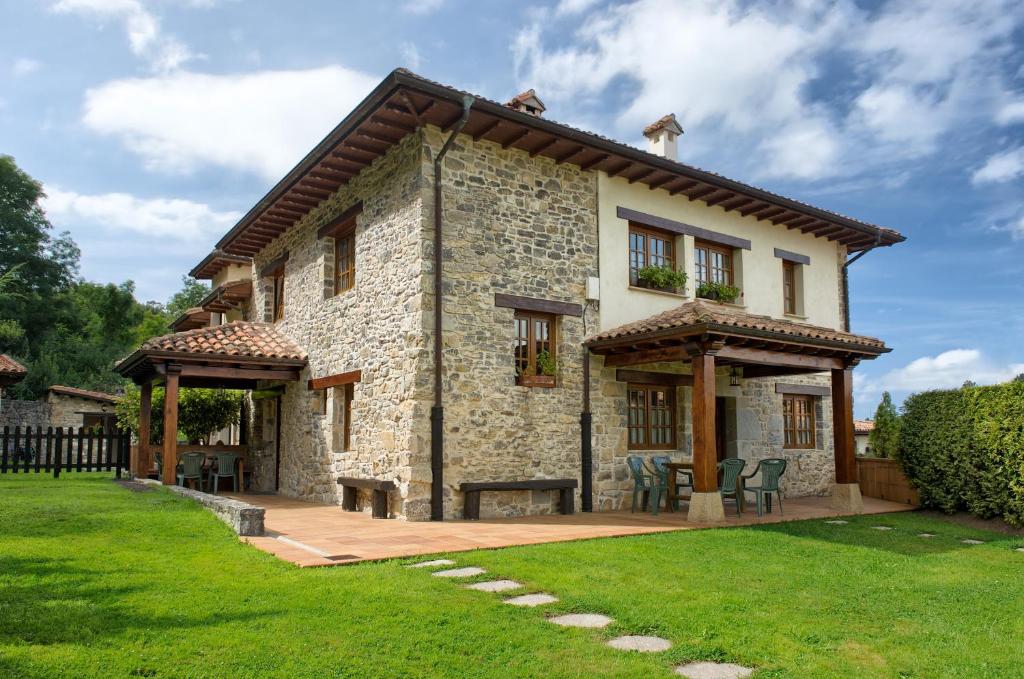 uma grande casa de pedra com um pátio e relva em Apartamentos El llugarón em Miravalles