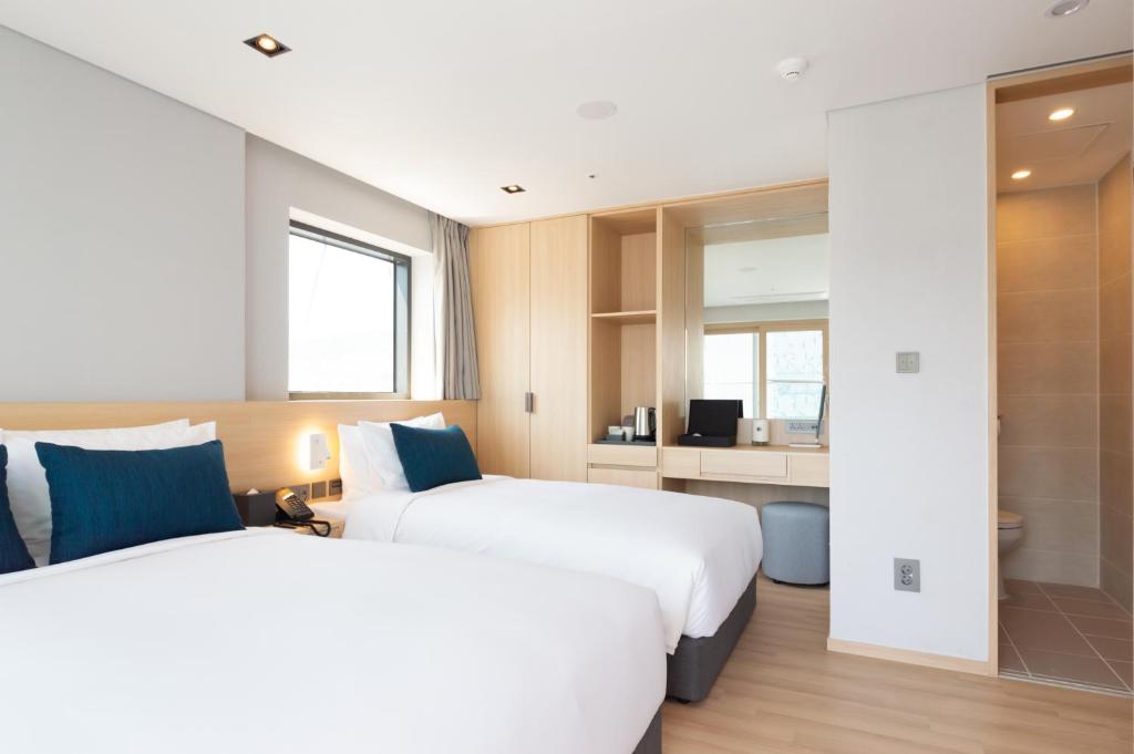 釜山にあるConnect Busan Hotel & Residenceのベッド2台とデスクが備わるホテルルームです。