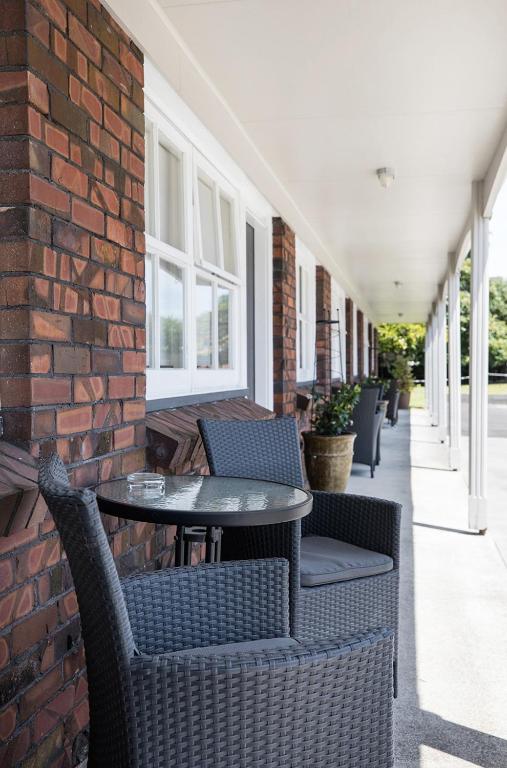 a patio with chairs and tables and a brick wall at Colonial Court Motor Inn in Tauranga