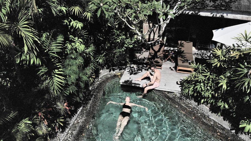 two people in a swimming pool with a dog in the water at JEstate villas & guest houses - Jimbaran in Jimbaran