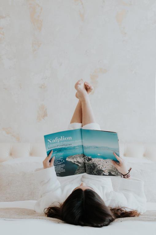 a woman laying on a bed reading a book at Castellano Hotel & Suites in Nafplio