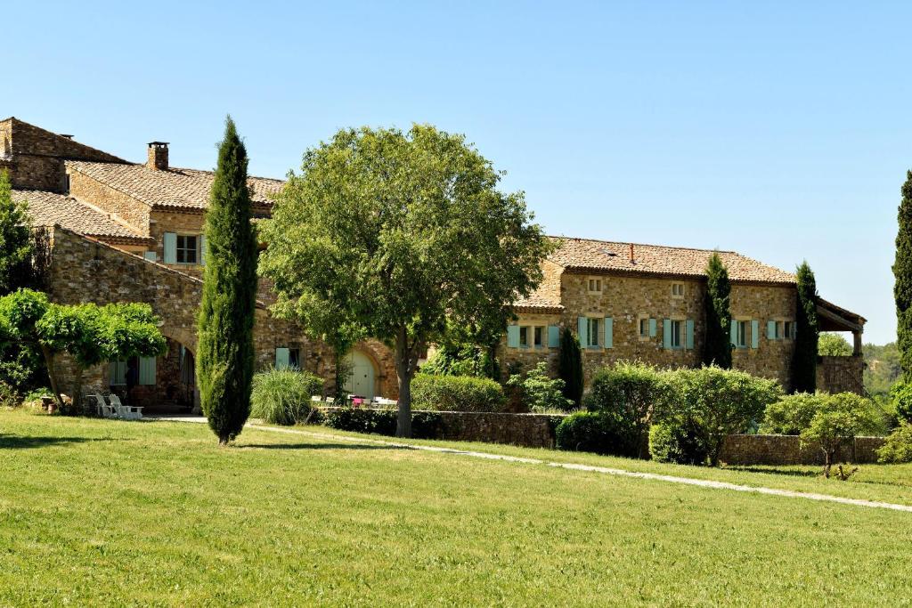 une grande maison en pierre avec une cour verdoyante dans l'établissement Mas la Buissonniere, à Aigaliers