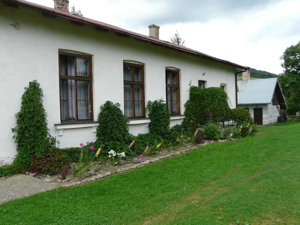 ein weißes Haus mit Büschen und Blumen im Hof in der Unterkunft Stara Szkoła in Krempna