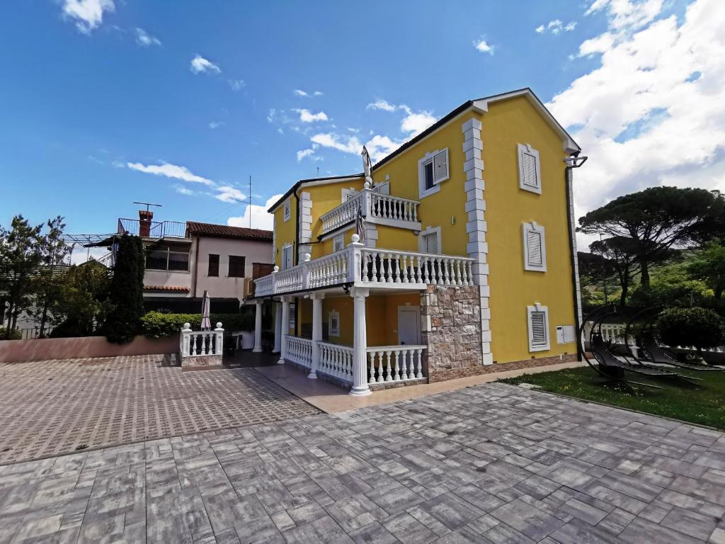 ein gelbes Haus mit einem Balkon auf einer Backsteineinfahrt in der Unterkunft Apartmaji ANA in Strunjan