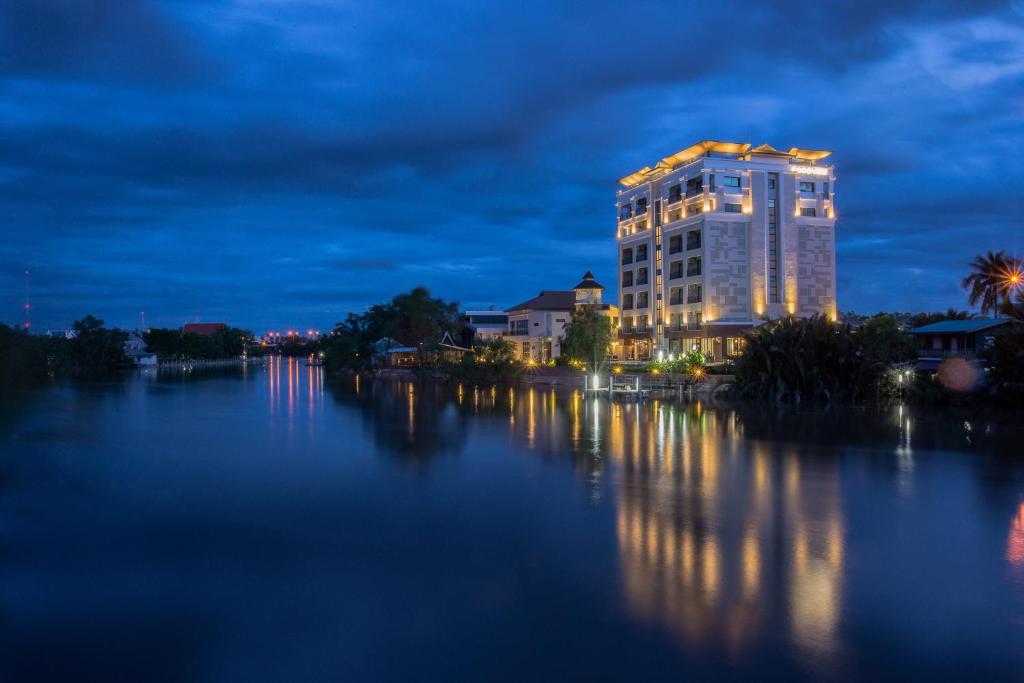 un edificio iluminado por la noche junto a un río en Coco View Hotel, en Samut Songkhram
