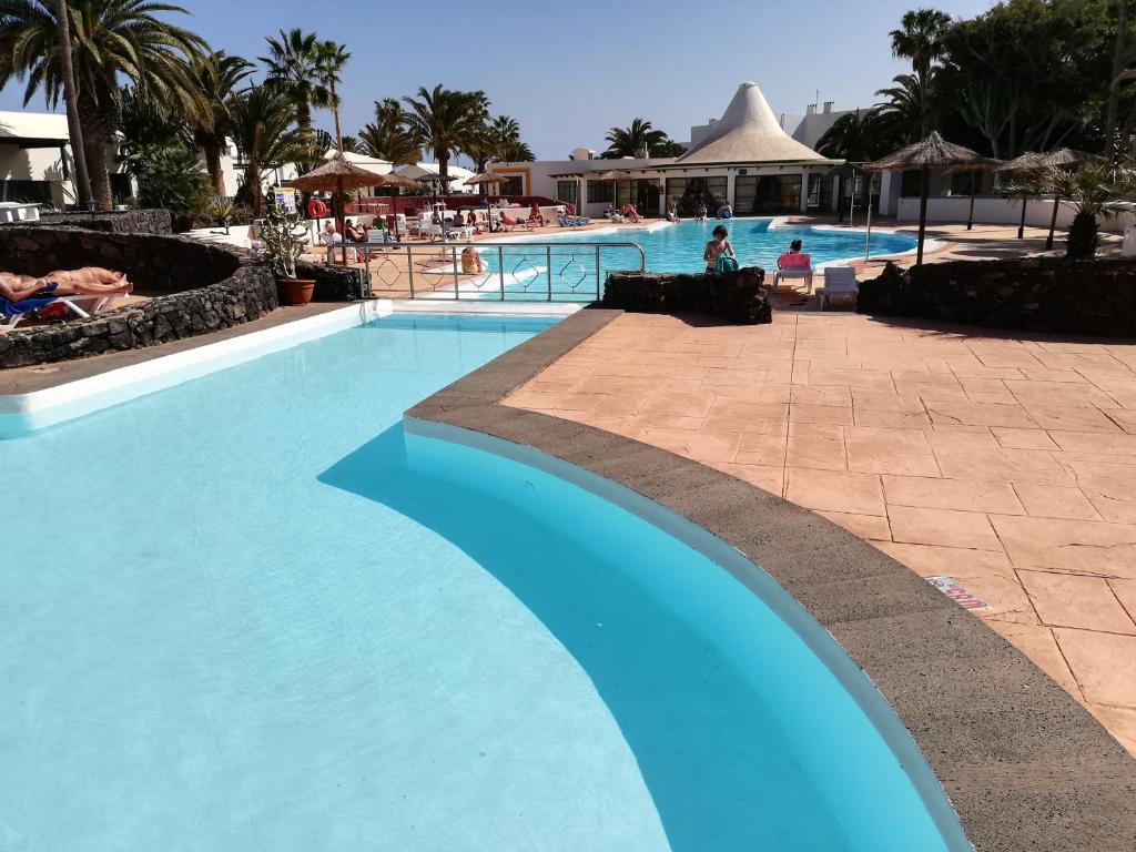 een zwembad in een resort met mensen op stoelen bij Apartamento DINO 10 PLAYA ROCA in Costa Teguise