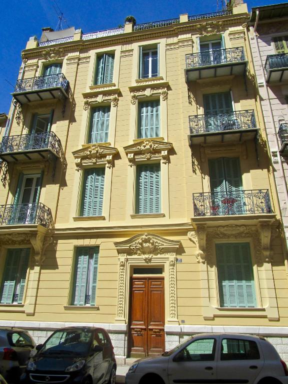 un grand bâtiment jaune avec deux voitures garées devant lui dans l'établissement Appartement, à Nice