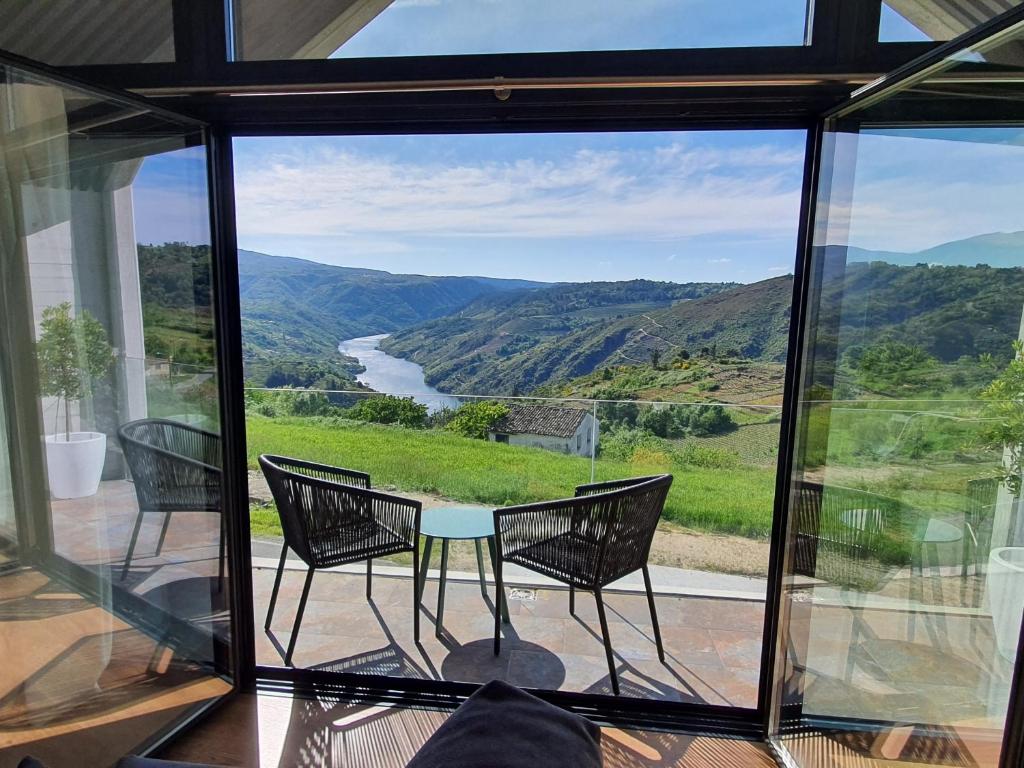 a glass room with a table and chairs and a view of a river at Miradores do Sil Hotel Apartamento in Cristosende