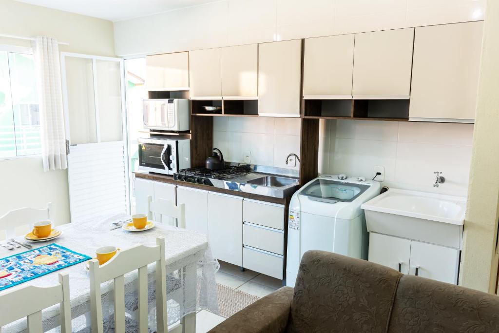 uma cozinha com armários brancos, uma mesa e um lavatório em Apto2 COM AR COND WI-FI E TV SMART em Itapema