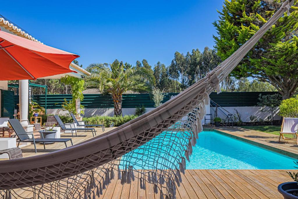 a hammock by a pool with chairs and an umbrella at Buganvilias Do Meco Guest house in Sesimbra