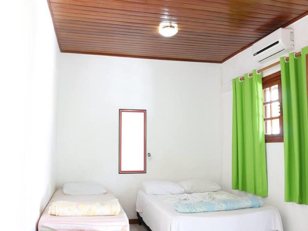 - 2 lits dans une chambre avec des rideaux verts dans l'établissement Pousada Trevo Do Barbuda, à Búzios