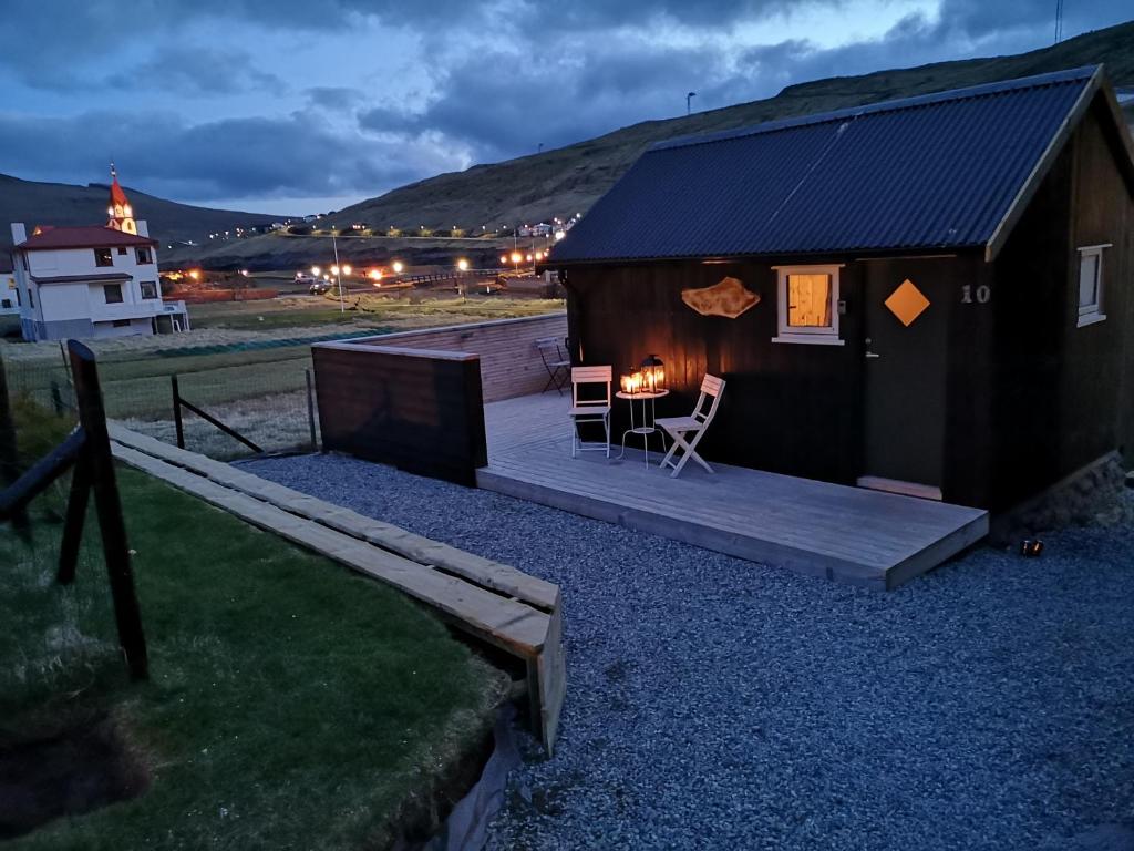 Cabaña pequeña con terraza de madera, mesa y sillas en Hjallurin, en Sandavágur