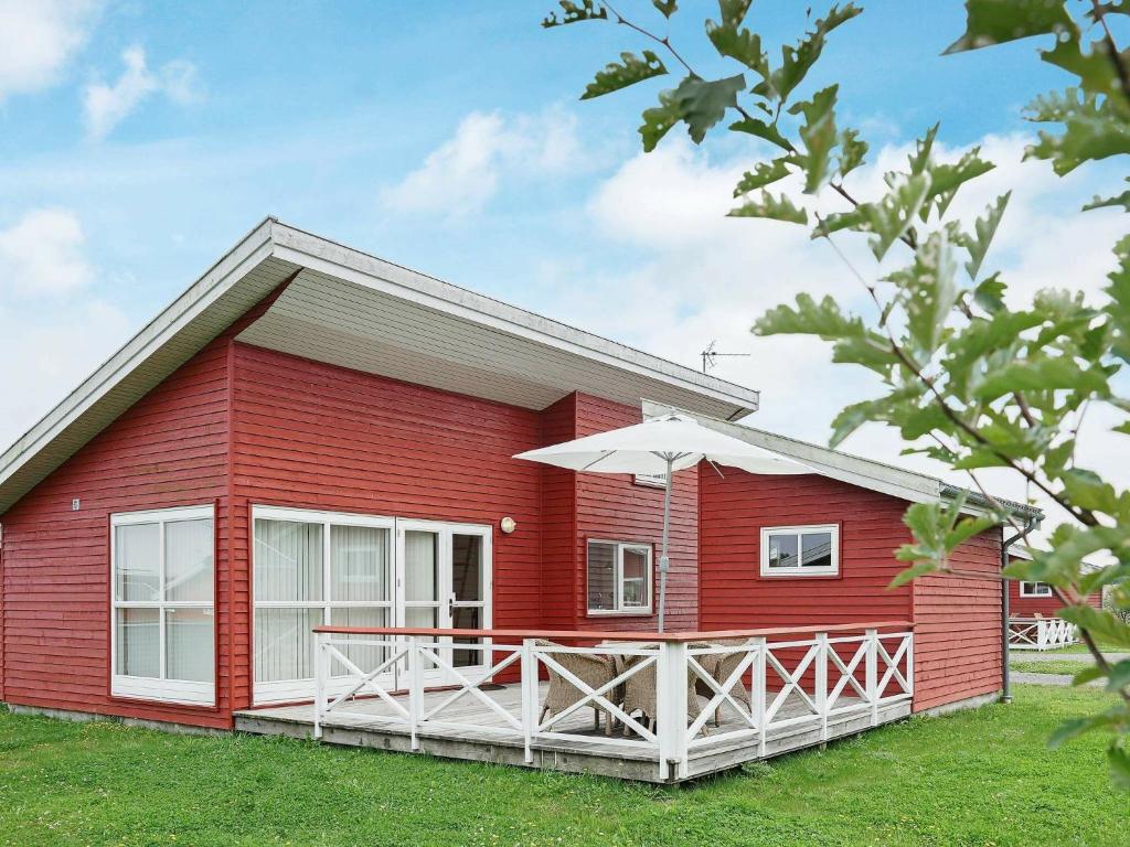 une maison rouge avec une terrasse et un parasol dans l'établissement 4 person holiday home in Gudhjem, à Gudhjem