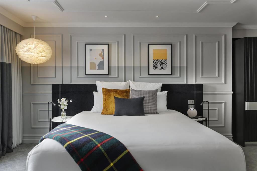Un dormitorio con una gran cama blanca y una lámpara de araña. en Fable Dunedin en Dunedin
