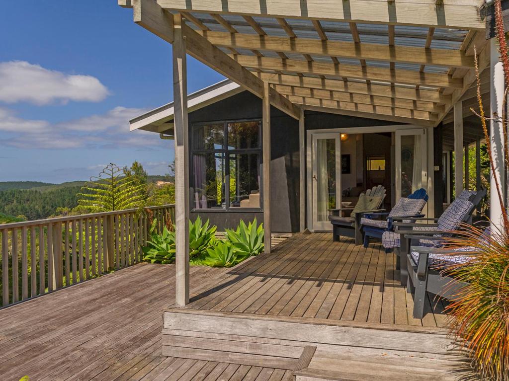 a wooden deck with chairs and a pergola at Hahei Hideaway - Hahei Holiday Home in Hahei