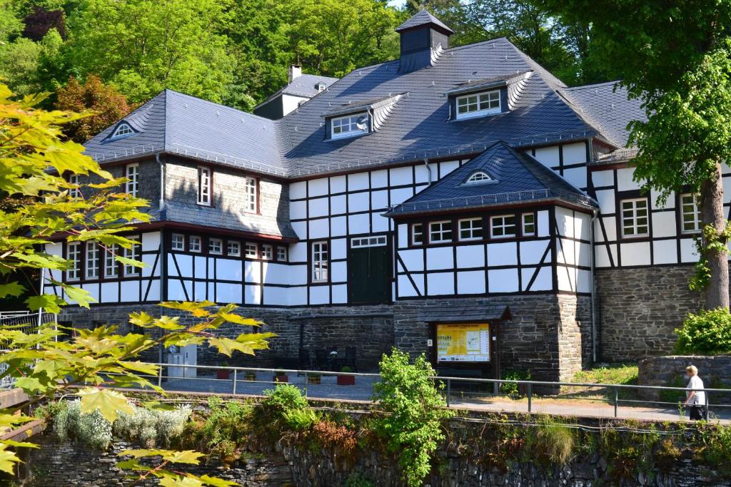 Une grande maison blanche et noire avec une femme debout devant elle dans l'établissement Villa Rur, à Monschau