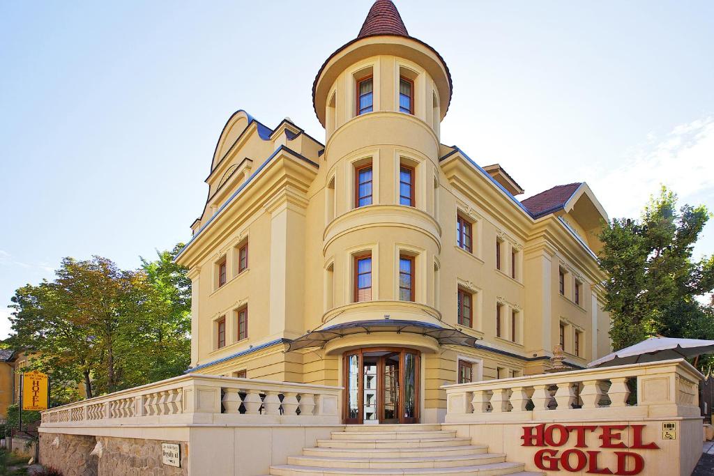 un gran edificio amarillo con una torre de reloj en la parte superior en Gold Hotel Budapest en Budapest