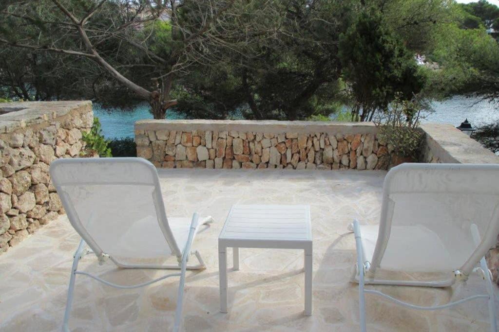 2 Stühle, ein Tisch und eine Steinmauer in der Unterkunft Sea frontline Apartment 'Charo' Pool and Wifi in Santanyi