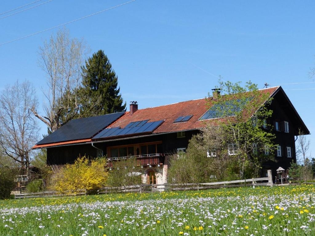 ein Haus mit Sonnenkollektoren auf dem Dach und einem Blumenfeld in der Unterkunft Ferienhof Hiemer in Sulzberg