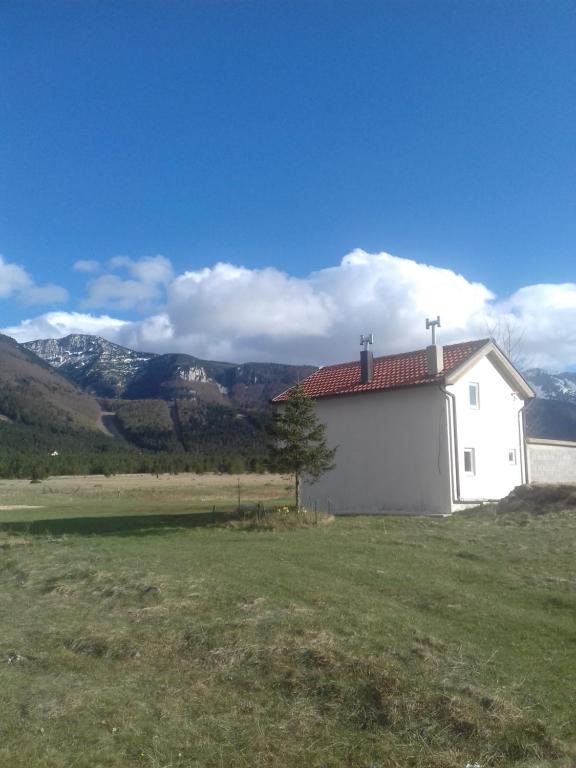 un bâtiment blanc dans un champ avec des montagnes en arrière-plan dans l'établissement Vikendica Jela Blidinje, à Rudo Polje