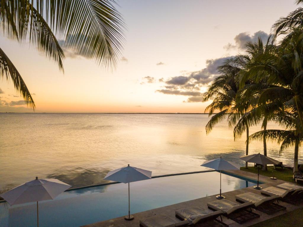 ein Pool mit Sonnenschirmen und das Meer bei Sonnenuntergang in der Unterkunft Casa Tortugas Boutique Hotel - CANCUN Hidden Gem in Cancún