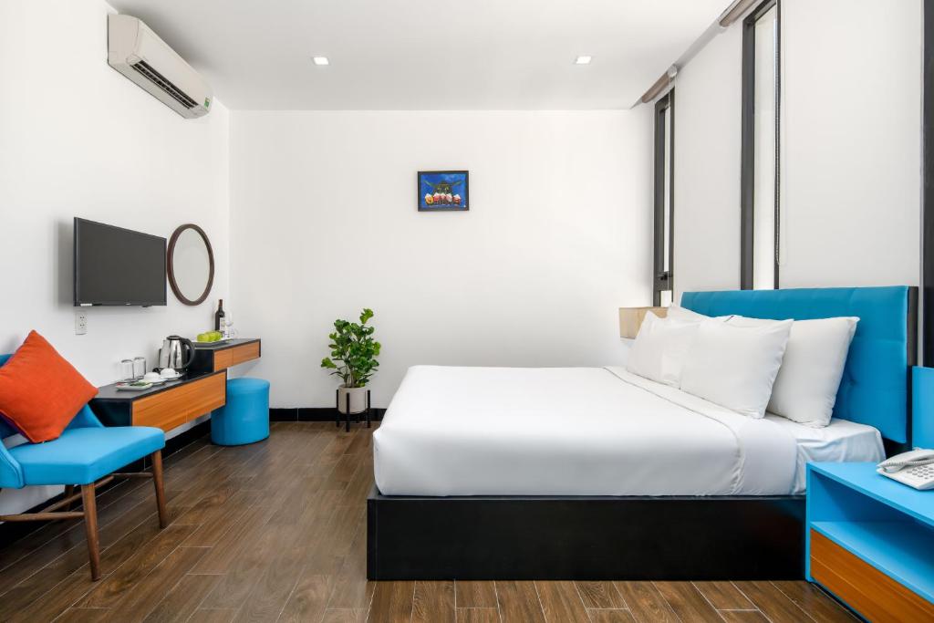 A staged double room with a blue headboard, television, beverage station and compact seating corner.