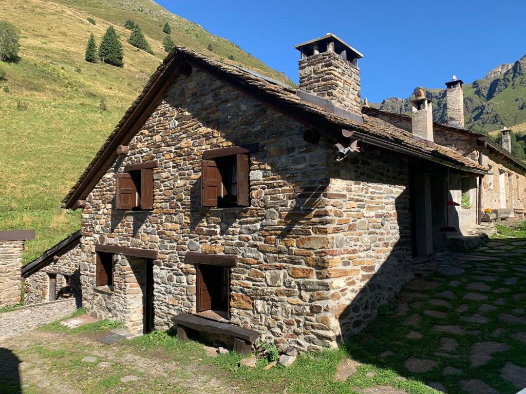 una vecchia casa in pietra con un camino su una collina di Baita Mirellina - Case di Viso a Ponte di Legno