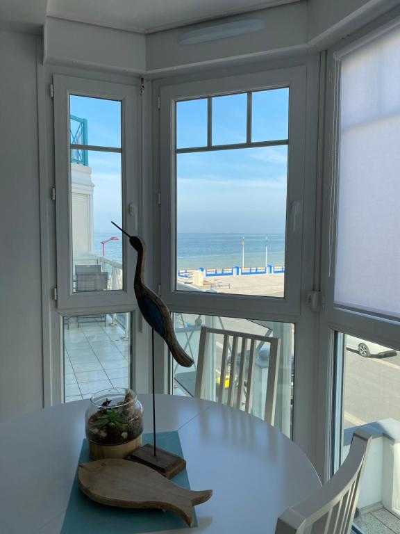 une statue d'oiseau assise sur une table devant les fenêtres dans l'établissement LE BON ENDROIT en bord de mer, vue mer , parking et wifi, à Wimereux