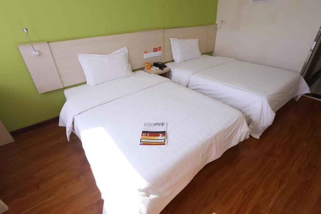 dwa łóżka w pokoju z białą pościelą i książką w obiekcie 7Days Inn Zhangjiakou Ming De North Road w mieście Zhangjiakou